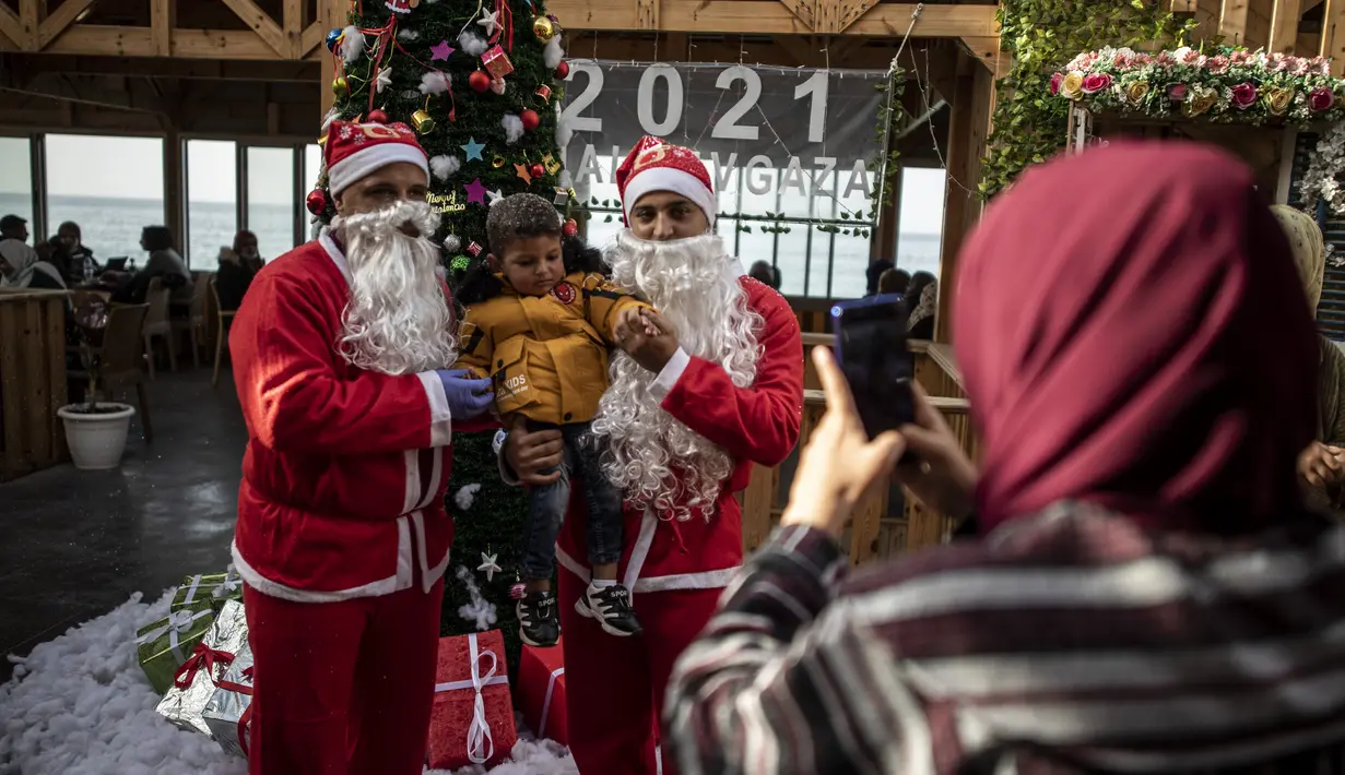 Pramusaji Palestina berpakaian Sinterklas menggendong seorang anak untuk berfoto di sebuah restoran di pantai di Kota Gaza, Minggu (13/12/2020). REstoran tersebut didandani dengan tema Natal, pelayanannya pun berpakaian seperti Sinterklas. (AP Photo/Khalil Hamra)