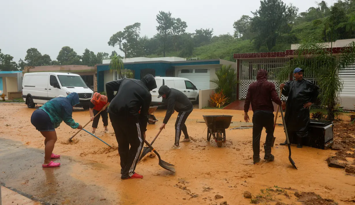 Orang-orang membersihkan puing-puing dari jalan setelah tanah longsor yang disebabkan oleh Badai Fiona di Cayey, Puerto Rico, Minggu, 18 September 2022. (AP Photo/Stephanie Rojas)
