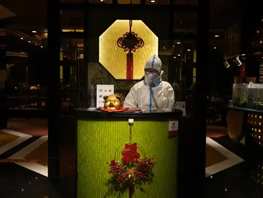 Mengenakan pakaian pelindung diri atau hazmat, seorang resepsionis restoran berbicara melalui telepon di Hotel Shangri-La pada Olimpiade Musim Dingin 2022, 16 Februari 2022, di Beijing. (AP Photo/Jae C.Hong)
