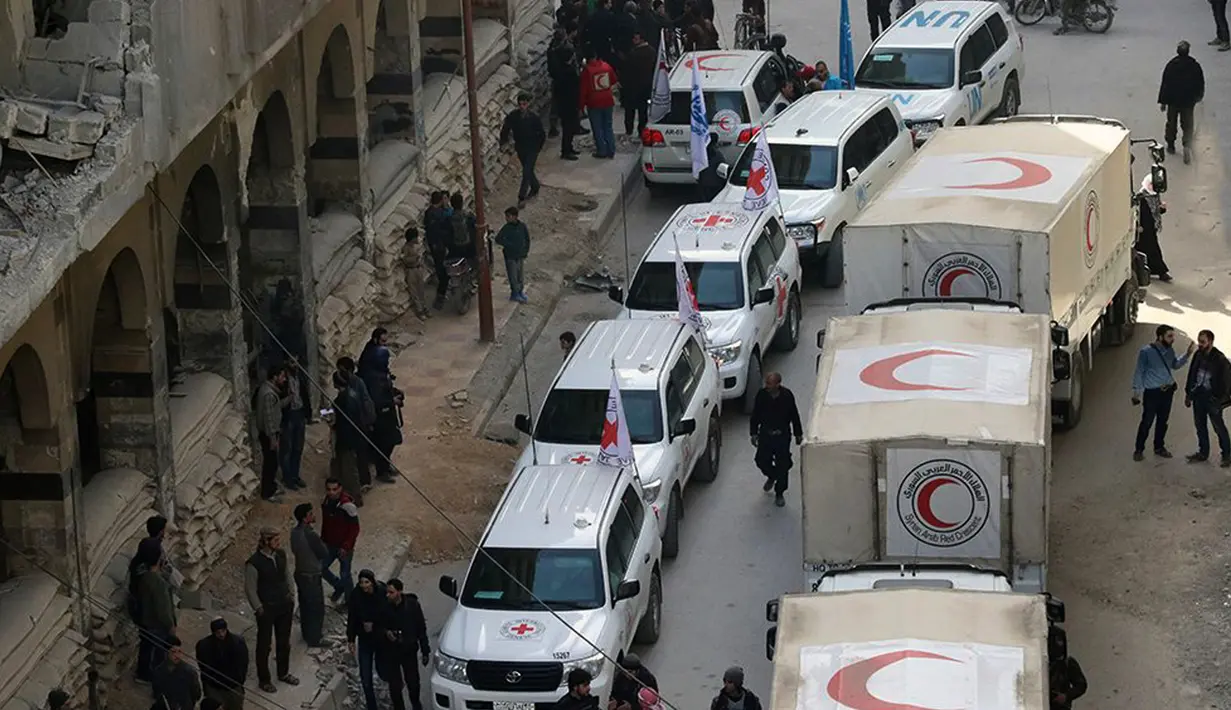 Warga sipil berkumpul di dekat konvoi truk bantuan Bulan Sabit Merah Suriah di Douma, Ghouta Timur, Damaskus, Suriah, Senin (5/3). Konvoi ini merupakan yang pertama sejak resolusi gencatan senjata pertengahan Februari lalu. (Syrian Red Crescent via AP)