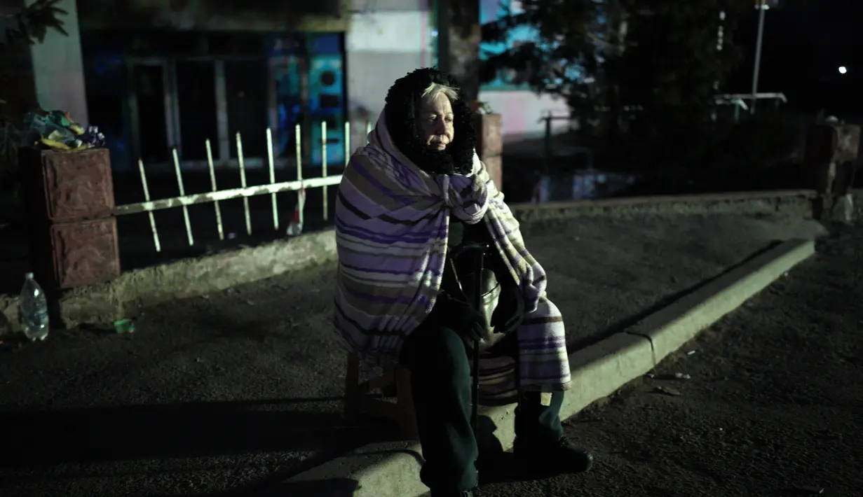 Seorang wanita pengungsi duduk di tepi jalan mendekati perbatasan dengan Polandia di Shehyni, Ukraina, Minggu (6/3/2022). Jumlah orang Ukraina yang dipaksa meninggalkan negara mereka meningkat menjadi 1,5 juta. (AP Photo/Daniel Cole)