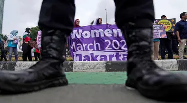 Seorang petugas polisi berjaga-jaga saat para aktivis membentangkan spanduk dalam unjuk rasa Hari Perempuan Internasional di Jakarta, Indonesia, Jumat, 8 Maret 2024. (AP Photo/Dita Alangkara)