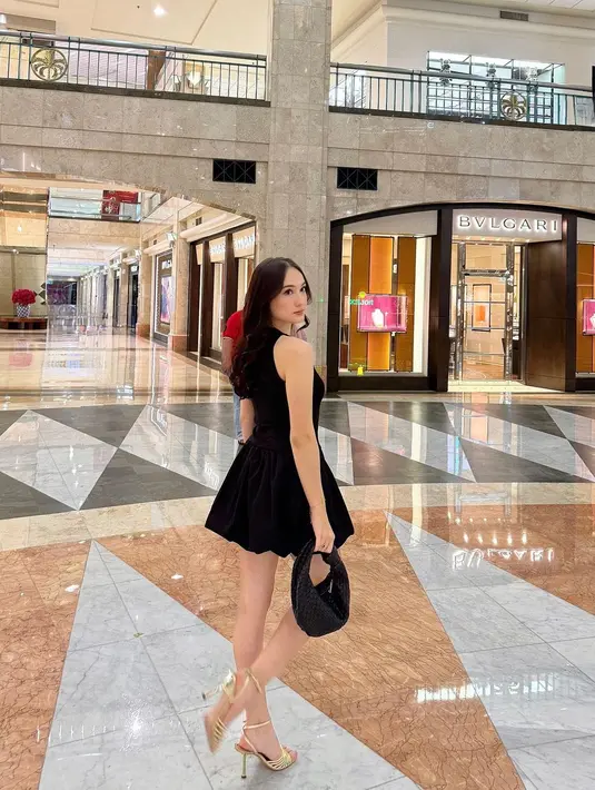 Mini dress tanpa lengan ini ia padukan dengan mini bag yang sama-sama berwarna hitam, dan high heels emas. [Foto: Instagram/its_lauramoane2]
