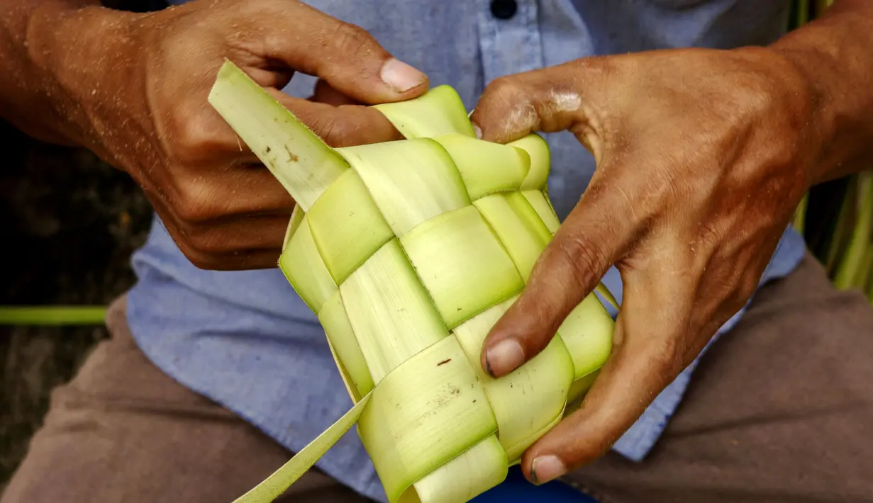 Seorang penjual menganyam daun kelapa atau kulit ketupat sambil menunggu pelanggan di sebuah pasar tradisional di Jakarta pada 2 April 2024. (BAY ISMOYO/AFP)