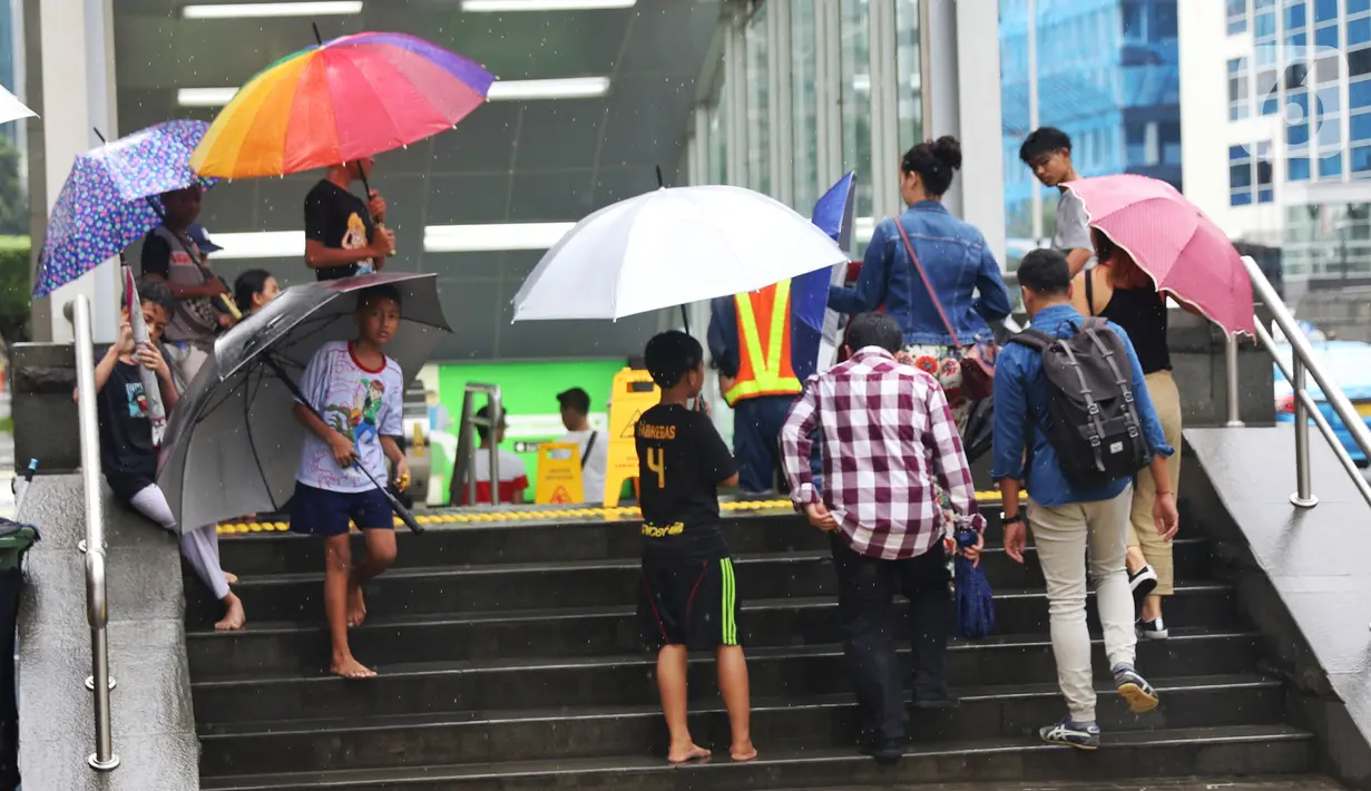 Anak-anak menawarkan jasa ojek payung di tengah hujan yang turun di kawasan Bundaran HI, Jakarta, Senin (3/2/2020). Hujan deras yang mengguyur sejumlah wilayah di DKI Jakarta dimanfaatkan para pengojek payung untuk mencari penghasilan tambahan. (Liputan6.com/Angga Yuniar)