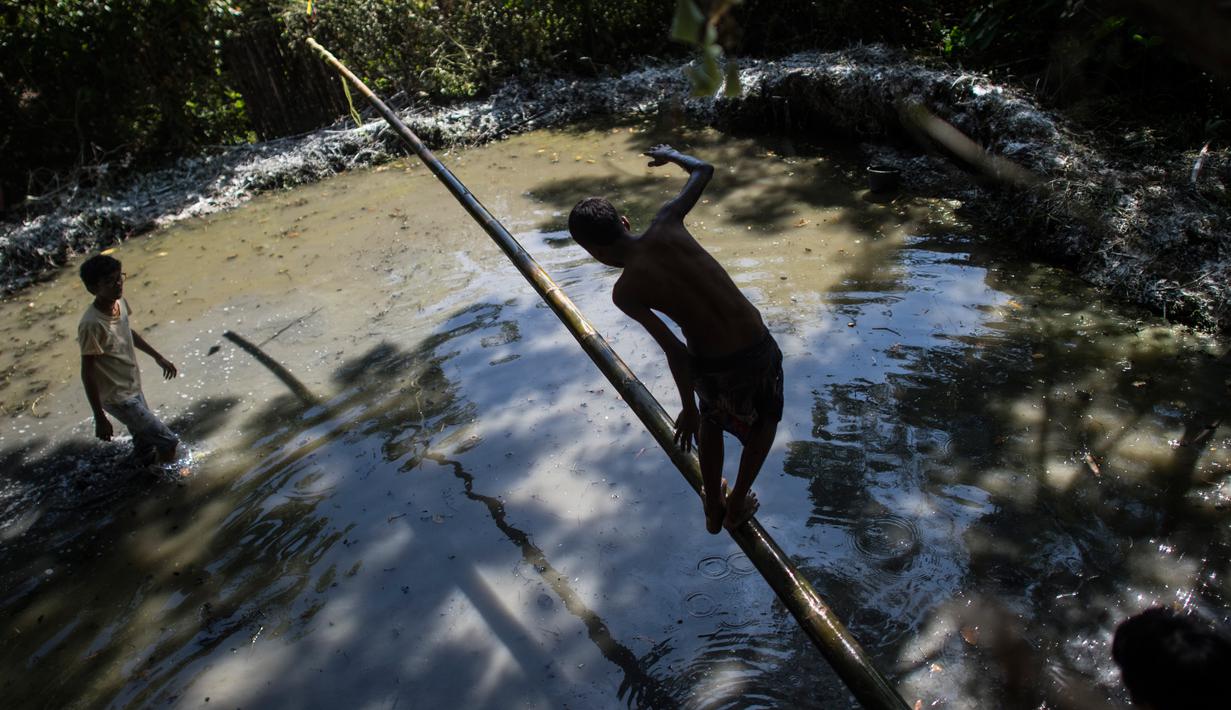 Seorang anak berjalan di atas tiang untuk mencoba meraih bendera nasional memperingati Hari Kemerdekaan Myanmar di pinggiran Yangon (4/1). Myanmar merayakan peringatan ke-71 deklarasi kemerdekaannya dari kolonial Inggris. (AFP Photo/Ye Aung Thu)