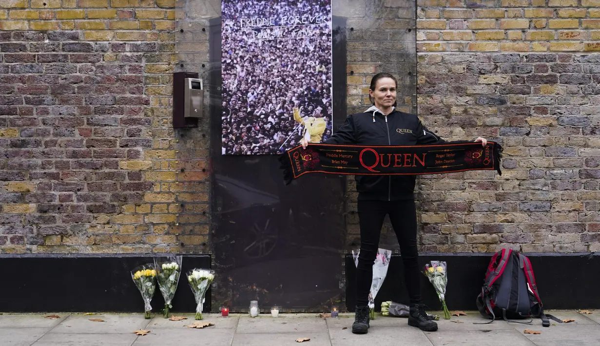 Penggemar memegang syal band rock Inggris Queen, saat berpose di luar rumah mendiang Freddie Mercury, pada peringatan 30 tahun kematiannya, di London, Rabu (24/11/2021). Freddie Mercury, penyanyi yang juga pentolan grup band Queen meninggal dunia pada 24 November 1991. (AP Photo/Alberto Pezzali)