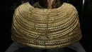 Seorang anggota staf berpose di sebelah jubah emas yang ditemukan di Mold in Wales, tertanggal 1600-1900 SM, dipajang di pameran The World of Stonehenge' di British Museum di London, Senin (14/2/2022). (AP Photo/Alastair Grant)