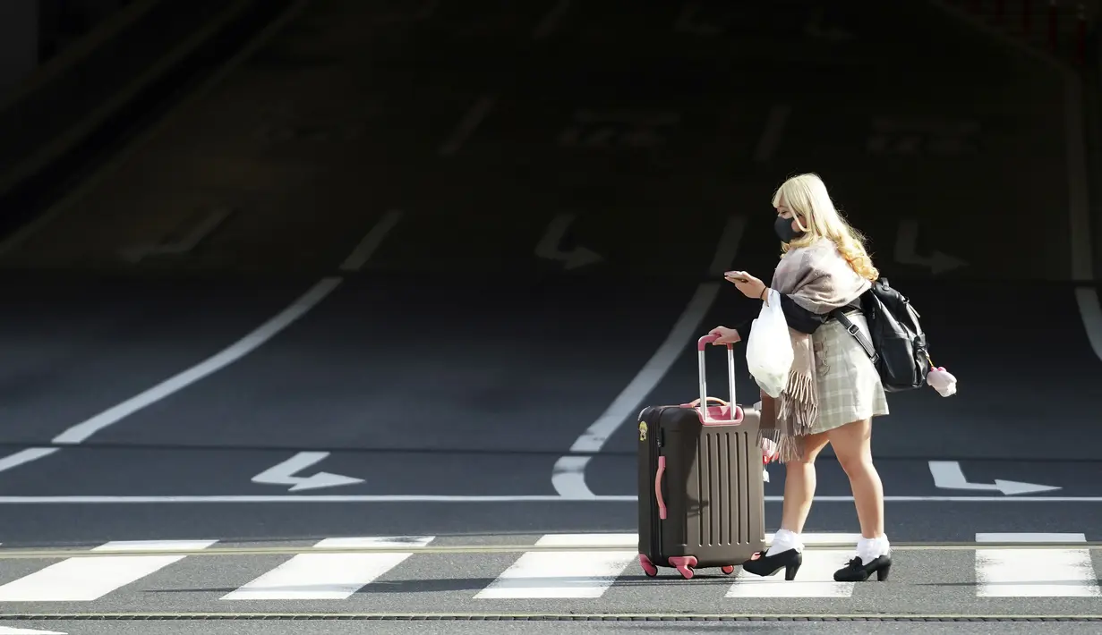 Seorang wanita yang mengenakan masker untuk membantu mencegah penyebaran virus corona berjalan di sepanjang penyeberangan pejalan kaki di Tokyo (17/3/2021). Ibukota Jepang mengonfirmasi lebih dari 400 kasus virus korona baru pada hari Rabu. (AP Photo/Eugene Hoshiko)