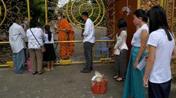 Warga antre untuk memberikan makanan dan sedekah kepada biksu Buddha saat Festival Pchum Ben (Festival Kematian) di luar pagoda di Phnom Penh, Kamboja, 24 September 2021. Pihak berwenang menghentikan perayaan Festival Kematian karena pandemi COVID-19. (TANG CHHIN Sothy/AFP)
