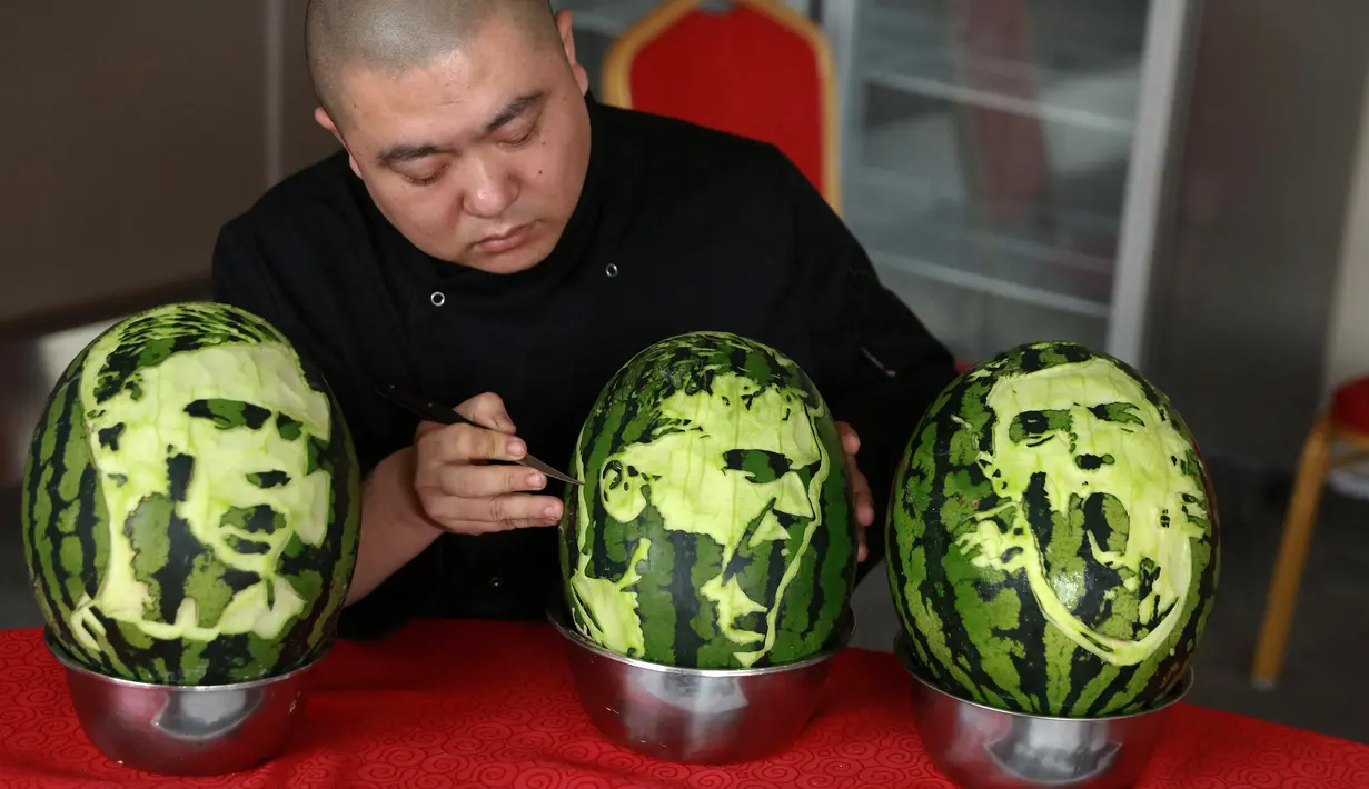 Seorang guru sekolah menengah mengukir wajah pemain sepak bola Prancis, Antoine Griezmann (tengah) pada buah semangka di Shenyang, Provinsi Liaoning, China, Senin (9/7). (AFP)