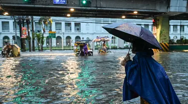 Orang-orang berjalan di sepanjang jalan yang tergenang banjir di Manila, Filipina pada 24 Juli 2024 di tengah hujan deras yang dibawa oleh Topan Gaemi. (Jam Sta Rosa/AFP)