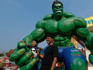 Seorang pria dan cucunya berpose dengan patung tokoh komik "Hulk" di kuil Tamru di provinsi Samut Prakan, Thailand, (3/3). Pihak Candi mengatakan telah menyiapkan patung-patung karakter komik Marvel untuk menarik pengunjung. (REUTERS/Chaiwat Subprasom)