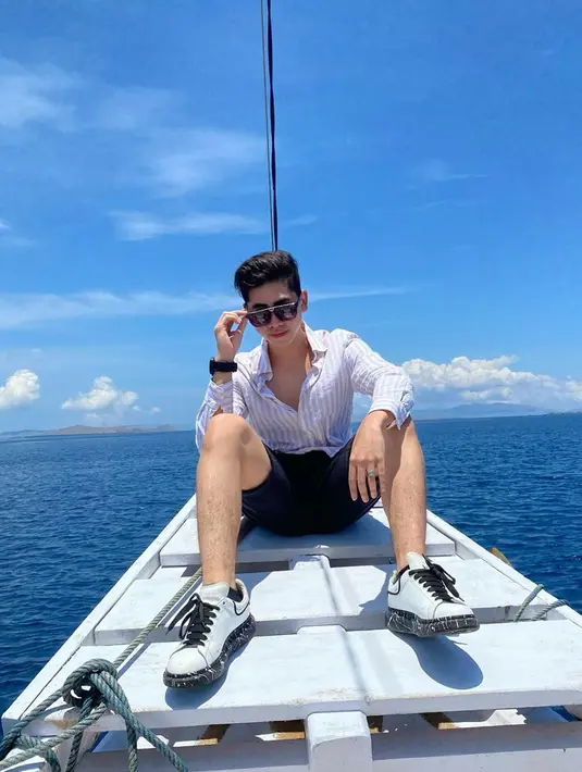 Tak hanya busananya, paras tampan Athalla Naufal semakin terpancar dengan mengenakan kacamat. Ketika duduk di atas kapal dengan pemandangan laut, ia terlihat menawan dengan kemeja putih dan celana pendek hitam serta sneakers.(Liputan6.com/IG/@ari_lasso)