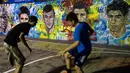 Dua remaja Brasil sedang bermain bola di dekat tembok lukisan wajah pemain top dunia, Brasil, Rabu (21/05/2014) (AFP PHOTO/Yasuyoshi CHIBA).