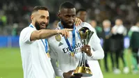 Penyerang Real Madrid Karim Benzema (kiri) dan bek Antonio Rudiger berselebrasi sambil memegang trofi Piala Dunia Antarklub 2022 usai mengalahkan Al Hilal dalam laga final di Prince Moulay Abdellah Stadium, Rabat, Minggu (12/2/2023) dini hari WIB. Los Blancos pun memegang rekor sebagai klub dengan gelar Piala Dunia Antarklub terbanyak. (FADEL SENNA / AFP)