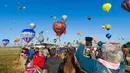 Pengunjung mengambil gambar ratusan balon udara yang terbang di pangkalan udara Chambley-Bussieres, Hagéville, Prancis, Senin (29/7/2019). Balon udara beragam warna mengikuti ajang ini. (Jean-Christophe VERHAEGEN/AFP)