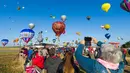 Pengunjung mengambil gambar ratusan balon udara yang terbang di pangkalan udara Chambley-Bussieres, Hagéville, Prancis, Senin (29/7/2019). Balon udara beragam warna mengikuti ajang ini. (Jean-Christophe VERHAEGEN/AFP)