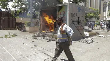 Seorang pria melintasi mesin ATM bitcoin bernama Chivo yang dibakar dalam protes terhadap Presiden Nayib Bukele di San Salvador, El Salvador, Rabu (15/9/2021). Ribuan warga Salvador berdemonstrasi menentang bitcoin, yang disahkan sebagai alat pembayaran oleh pemerintah. (AP Photo/Ivan Manzano)