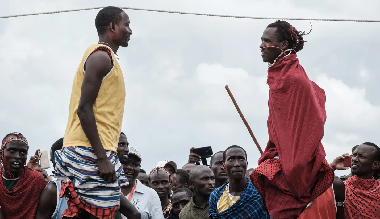 Dua pria melompat untuk mencapai tali selama mengikuti Olimpiade Maasai 2018 di Kimana, Kenya (15/12). Olimpiade Maasai ini untuk menghentikan berburu singa. (AFP Photo/Yasuyoshi Chiba)