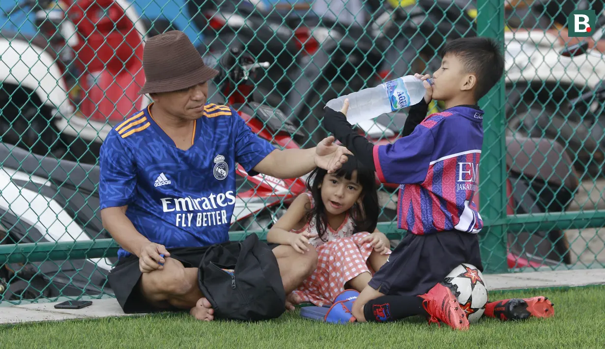 Tidak hanya Ibu-ibu, seorang bapak pun ikut hadir di lapangan. Tampak seorang anak sedang meminum air yang diberikan bapaknya. (Bola.com/M Iqbal Ichsan)