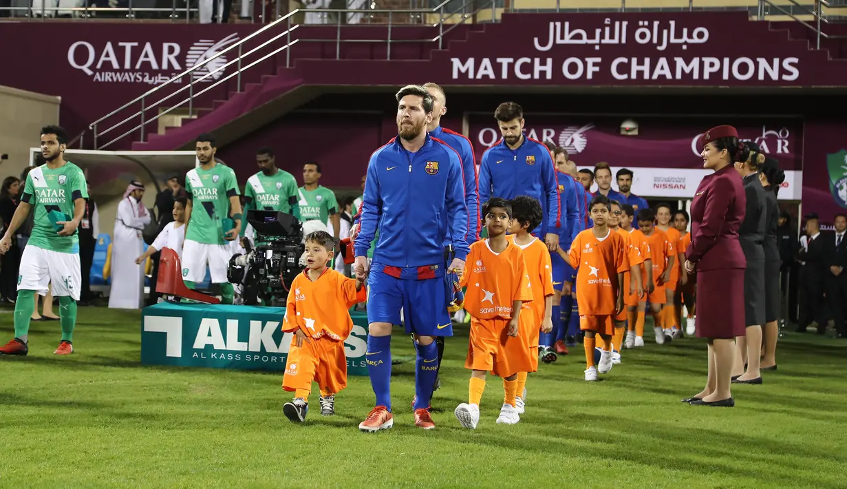 Bintang Barcelona Lionel Messi menggandeng bocah Afghanistan, Murtaza Ahmadi (kiri) saat memasuki lapangan sebelum pertandingan persahabatan melawan Al-Ahli di ibu kota Qatar, Doha, Selasa (13/12). (Karim Jaafar/AFP)