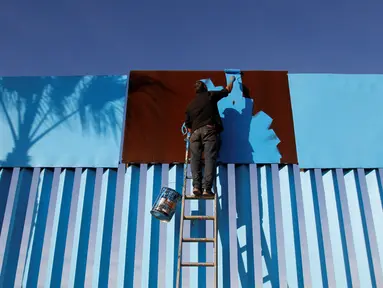 Seorang seniman menyelesaikan pengecatan pagar yang memisahkan antara Meksiko dan Amerika Serikat di Playas Tijuana, Meksiko (10/12). (Reuters/Jorge Duenes)