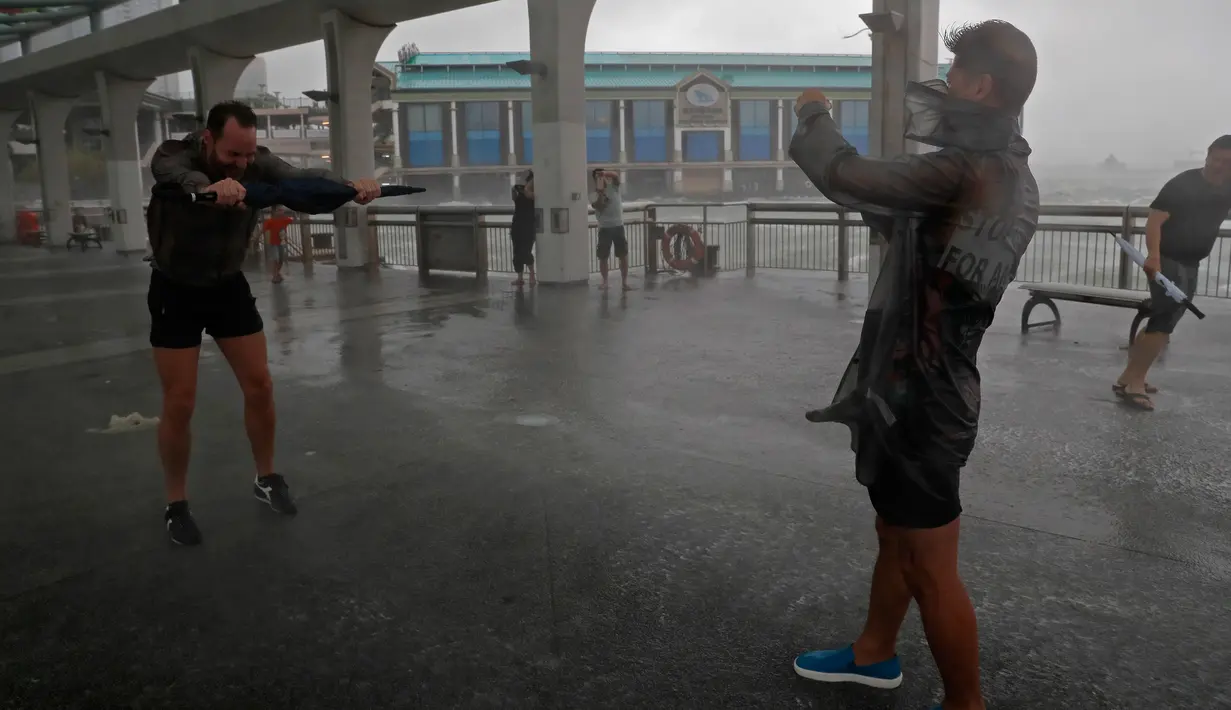 Sejumlah warga bermain saat angin kencang yang disebabkan oleh angin topan Hato di tepi pantai Victoria Habour di Hong Kong, (23/8). Embusan angin akibat topan Hato mencapai kecepatan 86 kilometer hingga 103 kilometer per jam. (AP Photo/Vincent Yu)