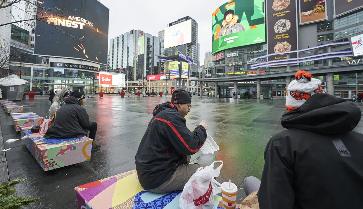 Orang-orang menikmati makan siang mereka di bangku di Yonge-Dundas Square di Toronto, Ontario, Rabu (5/1/2022). Provinsi Ontario menutup restoran untuk makan di tempat di tengah kesibukan pembatasan baru guna membendung penyebaran varian Omicron Covid-19. (Geoff Robins / AFP)