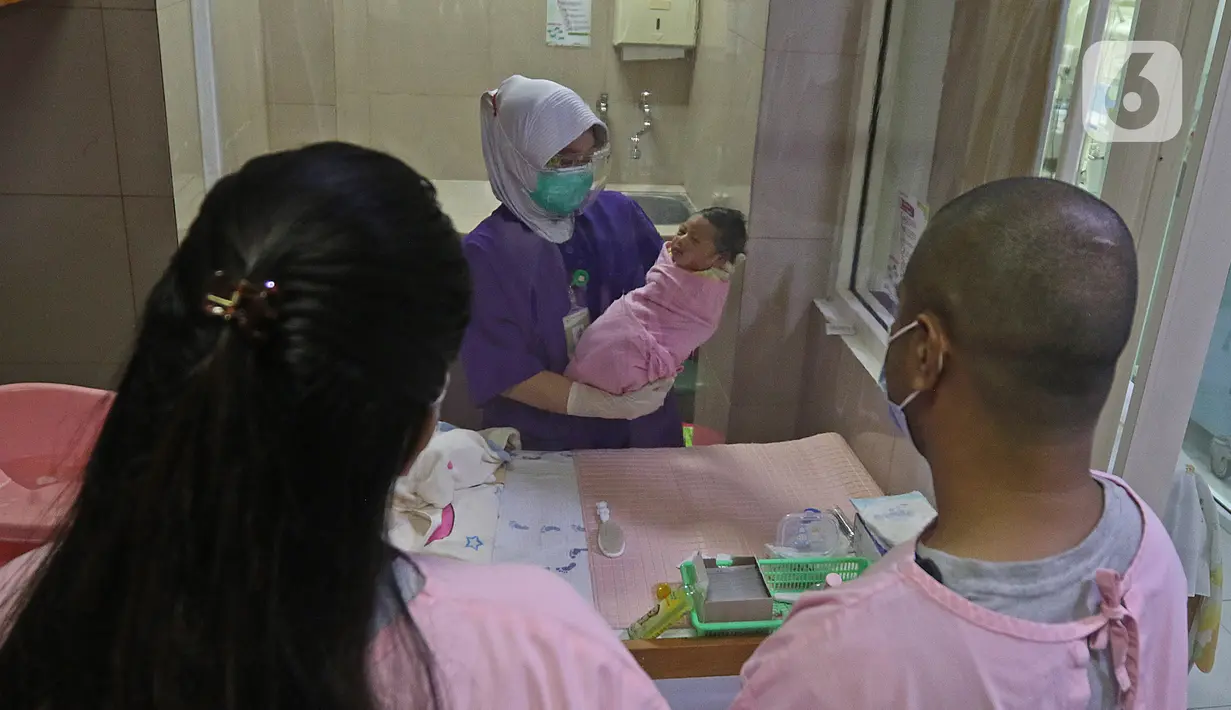 Perawat menunjukkan seorang bayi kepada orangtuanya setelah selesai dimandikan di RSIA Tambak, Jakarta, Kamis (18/02/2021). Melatih para ibu baru untuk memandikan bayi pertama tersebut dilakukan dengan menerapkan protokol kesehatan ketat. (Liputan6.com/Herman Zakharia)