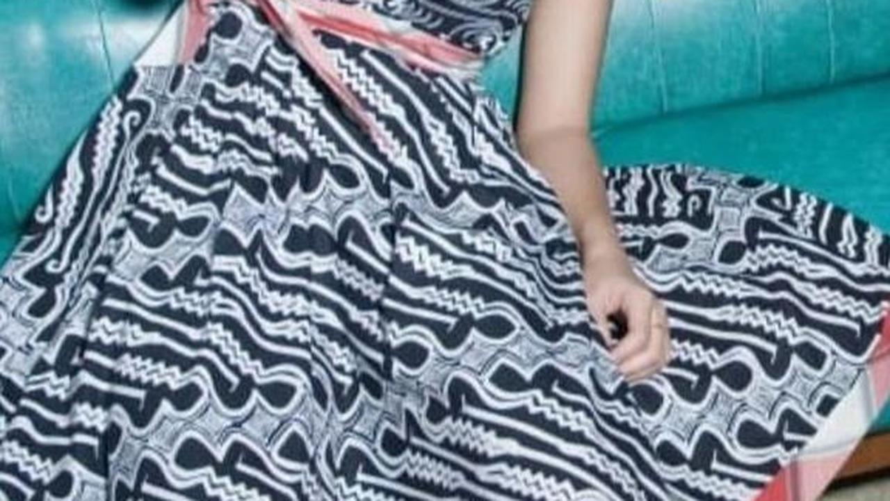 Dian tampil anggun mengenakan gaun batik modern berwarna hitam dan putih, dengan motif geometris yang memikat, sambil duduk dalam pose santai.<br>