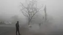 Seseorang melintasi persimpangan ketika petugas menyapu jalan di tengah kabut tebal di New Delhi, Senin (30/12/2019). New Delhi, ibu kota India, saat ini mengalami musim dingin dengan hari dingin terpanjang dalam 22 tahun terakhir. (AP Photo/Manish Swarup)