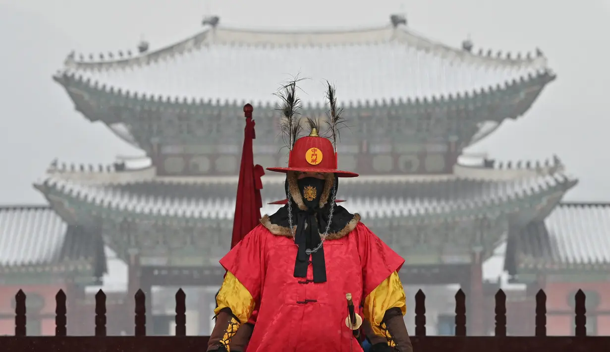 Seorang 'penjaga istana' berdiri untuk turis di depan Istana Gyeongbokgung yang tertutup salju di pusat kota Seoul (19/1/2022). Pihak berwenang di Seoul dan daerah sekitarnya pada Rabu (19/1) tetap waspada karena wilayah ibu kota diperkirakan akan turun salju lebat sepanjang hari. (AFP/Jung Yeon-je)