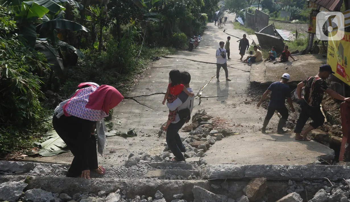 Sejumlah warga melintasi jalan yang terbelah akibat pergeseran tanah di kawasan Bojong Koneng, Babakan Madang, Kabupaten Bogor, Jawa Barat, Jumat (16/9/2022). Badan Penanggulangan Bencana Daerah (BPBD) setempat mencatat 18 unit rumah mengalami kerusakan, dan pergeseran tanah itu menyebabkan retakan-retakan di tanah, dinding, plafon dan lantai rumah warga serta akses jalan sudah tidak bisa dilewati oleh kendaraan roda dua dan roda empat. (Liputan6.com/Herman Zakharia)