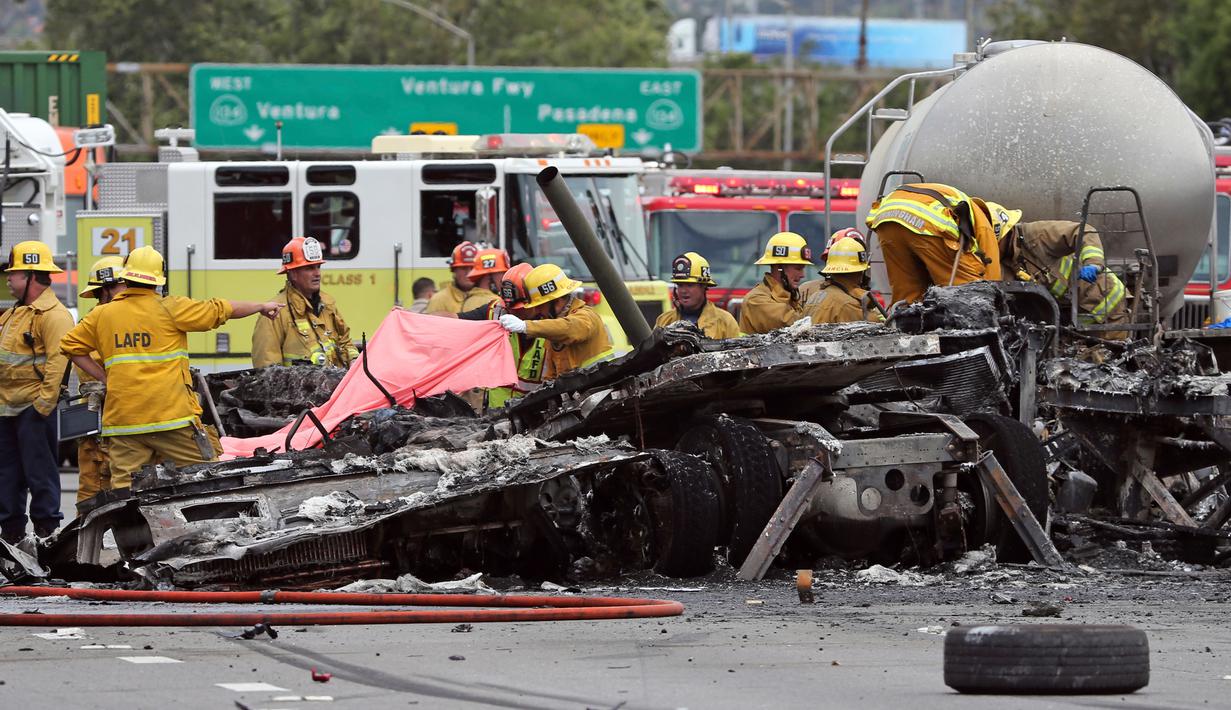 Sejumlah petugas mengevakuasi bangkai truk yang telah hangus usai terjadi tabrakan antara dua truk besar di utara pusat kota Los Angeles (25/4). Kecelakaan ini juga membuat kemacetan panjang di wilayah tersebut. (AP Photo/Reed Saxon)