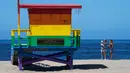 Dua wanita berselfie di dekat menara penjaga pantai Venice Pride Flag di daerah Venice Beach, Los Angeles (13/5/2020). Los Angeles County membuka kembali pantai-pantainya pada Rabu dalam pelonggaran terbaru pembatasan coronavirus. (AP/Mark J. Terrill)