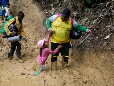 Seorang Pria dari kelompok migran membantu anak yang terjartuh dilumpur saat berjalan melintasi Celah Darien dari Kolombia ke Panama, Sabtu, (15/10/2022). Perjalanan Kelompok Imigran tersebut berharap mencapai Amerika Srikat (AS).(Fernando Vergara/AP)