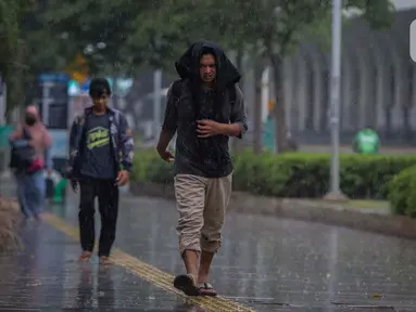 Warga menutupi kepala dari guyuran hujan saat melintasi kawasan Sudirman, Jakarta, Kamis (4/1/2024). (Liputan6.com/Angga Yuniar)