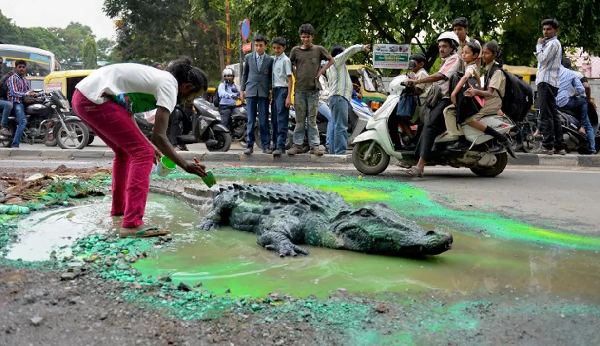 Seniman Baadal Nanjundaswamy saat menyelesaikan boneka buaya di atas jalan berlubang di Sultanpalya, Bangalore, India, Kamis (18/6/2015). Aksi protes tersebut untuk mendesak pemerintah agar segera memperbaiki jalan yang rusak. (AFP PHOTO/ Manjunath KIRAN)