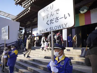 Penjaga keamanan memegang tanda untuk mengontrol pengunjung yang berjalan untuk berdoa memohon keberuntungan selama "hatsumode" atau kunjungan pertama tahun ini ke kuil atau wihara, di kuil Kawasaki Daishi di Kawasaki, dekat Tokyo, Senin, 2 Januari 2023. (AP Photo/Eugene Hoshiko)