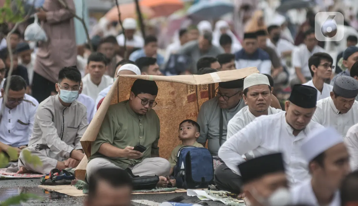 Jemaah melindungi kepala dari hujan saat menunaikan Salat Idul Fitri 1444 H di halaman Jakarta International Equestrian Park, Pulomas, Jakarta Timur, Jumat (21/4/2023). (merdeka.com/Iqbal S Nugroho)
