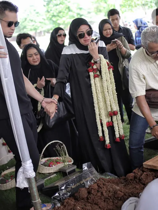 Aufar Hutapea menggenggam tangan sang istri, Olla Ramlan saat proses pemakaman sang ayahanda, Muhammad Ramlan di TPU Tanah Kusir, Jakarta, Selasa (5/6). Ayahanda Olla Ramlan meninggal akibat kanker dan liver yang dideritanya. (Liputan6.com/Faizal Fanani)