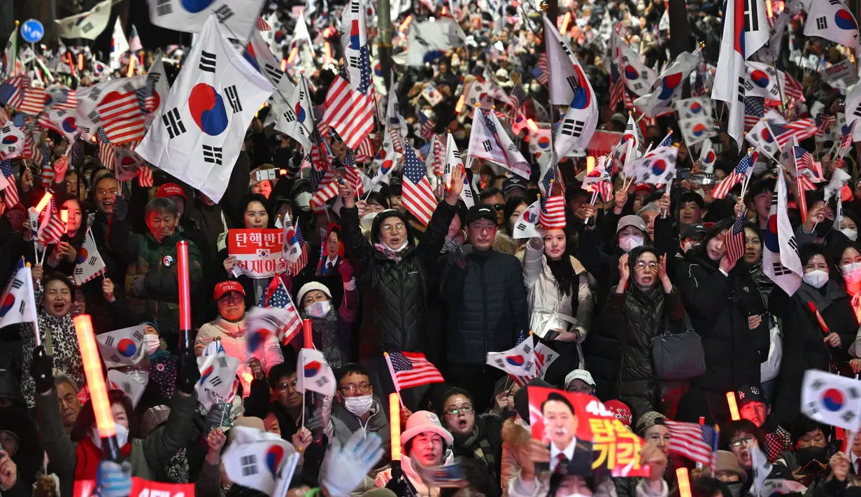 Para pendukung Yoon Suk Yeol melambaikan bendera Korea Selatan dan Amerika Serikat dalam sebuah unjuk rasa di dekat kediaman presiden di Seoul pada tanggal 8 Maret 2025, setelah iring-iringan mobil yang membawa Yoon tiba di kediaman tersebut. (Jung Yeon-je/AFP)