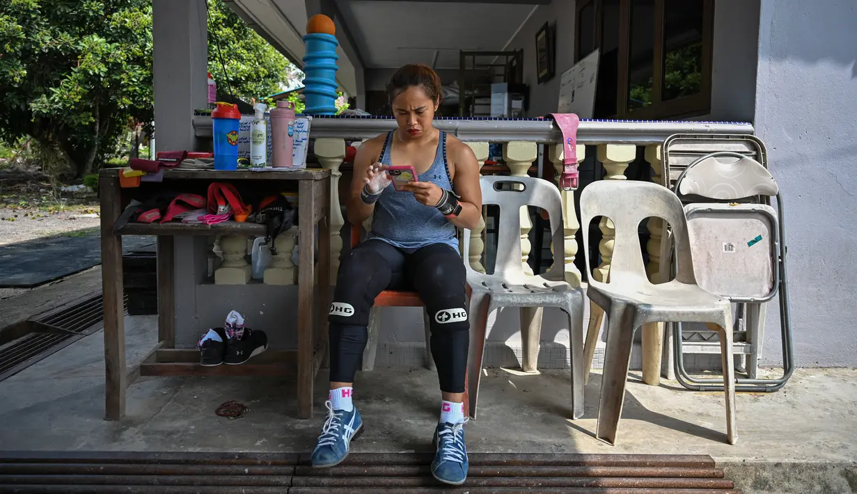 Atlet angkat besi Olimpiade Filipina, Hidilyn Diaz memeriksa pesan pada ponselnya selama sesi Latihan di Jasin di kota Malaka, Malaysia pada 21 Mei 2021. Diaz (30) yang memenangkan perak di Rio 2016 lalu telah tertahan di Malaysia sejak Februari 2020 karena pandemi virus corona. (Mohd RASFAN/AFP)