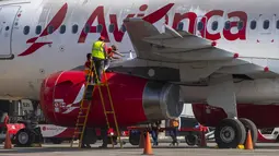 Pekerja menutupi bagian-bagian motor pesawat dengan plastik untuk mencegah abu vulkanik masuk di bandara internasional La Aurora yang telah ditutup akibat letusan di gunung berapi Pacaya di Guatemala City (23/3/2021). (AP Photo / Moises Castillo )