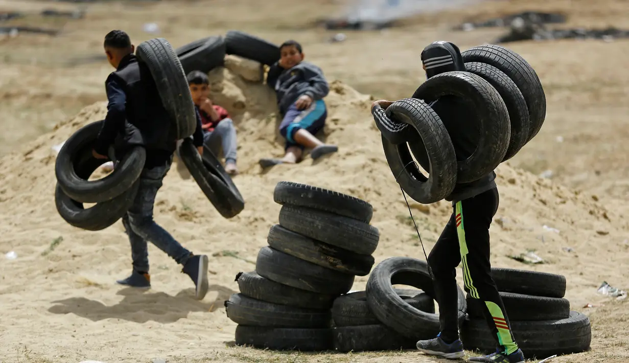 Sejumlah pemuda Palestina membawa ban untuk dibakar saat menggelar aksi di perbatasan Palestina-Israel di kota Gaza tengah (13/4). Mereka melakukan aksi tersebut menyusul tewasnya 33 orang Palestina akibat serangan tentara Israel. (AFP/Mohammed Abed)