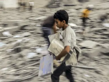 Seorang anak berjalan pergi dengan barang-barang yang diselamatkan dari reruntuhan bangunan yang terkena serangan Israel di Rafah di Jalur Gaza selatan pada 15 Oktober 2023. (Photo by MOHAMMED ABED / AFP)