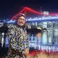 Yogi menggunakan baju khas Jawa pada Senin malam sambil mengabadikan momen bersejarah dengan jembatan Brisbane yang berwarna merah putih. (Facebook. Agustinus Jogiono)