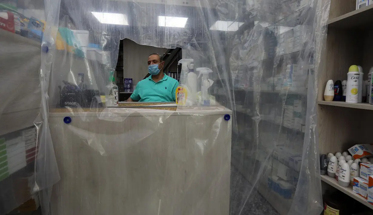 Pegawai terlihat dari balik lapisan plastik untuk mengurangi kontak fisik di sebuah apotek di Baghdad, Irak, Selasa (14/4/2020). Dari 1.400 kasus virus corona COVID-19 yang terkonfirmasi di Irak, 78 orang di antaranya meninggal dunia. (Xinhua)