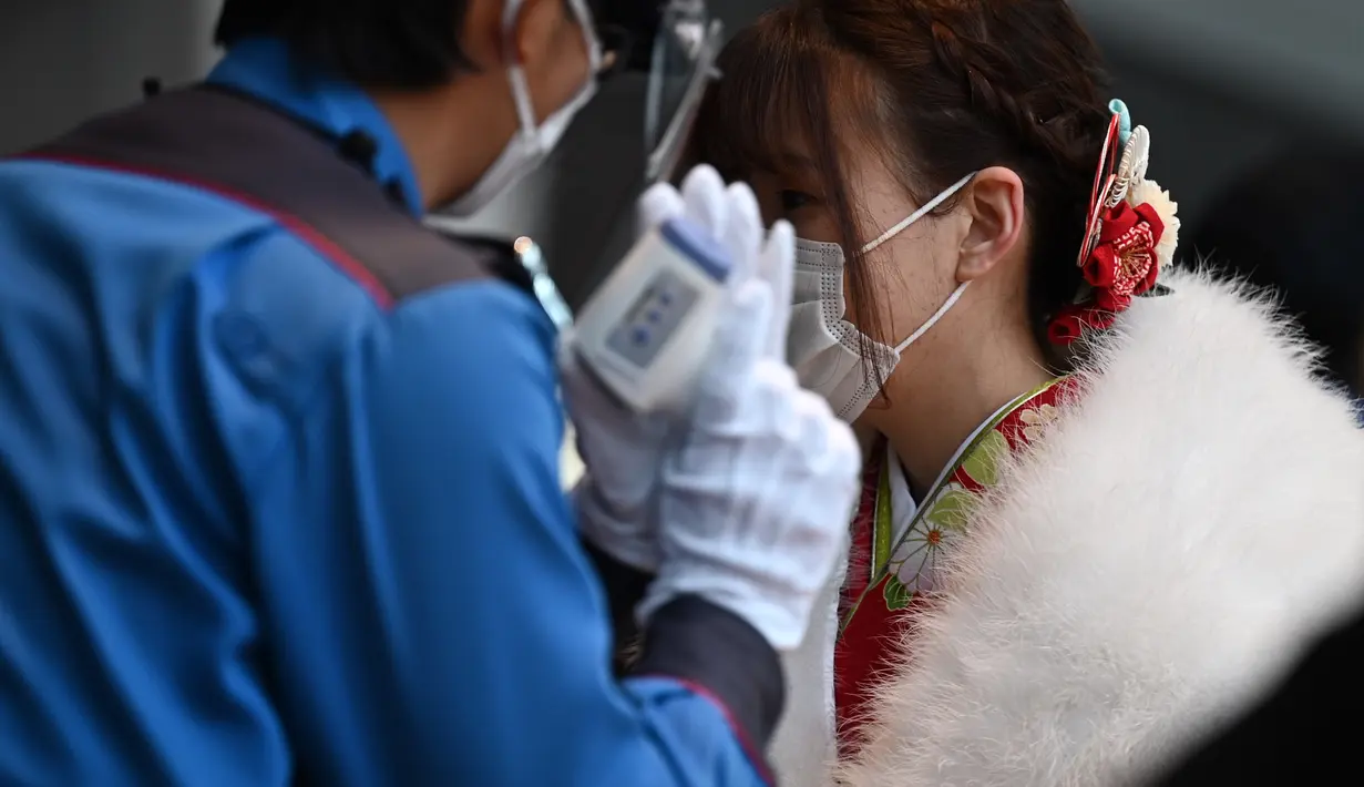 Seorang wanita berusia dua puluh tahun mengenakan kimono diperiksa suhu tubuhnya di pintu masuk Yokohama Arena untuk menghadiri upacara perayaan "Coming-of-Age Day" di Kawasaki, prefektur Kanagawa (11/1/2021). (AFP/Philip Fong)